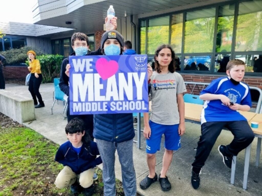students holding a sign that says "we love meany middle school"